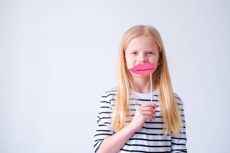 funny child blonde girl with red paper lips on grey background. Copyspace. Happy mother day. Birthday partyの写真素材