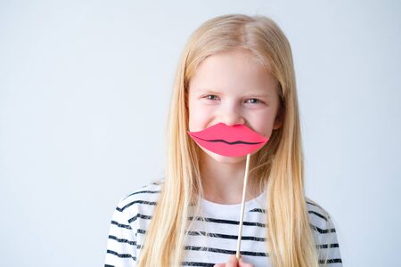 funny child blonde girl with red paper lips on grey background. Copyspace. Happy mother day. Birthday partyの写真素材