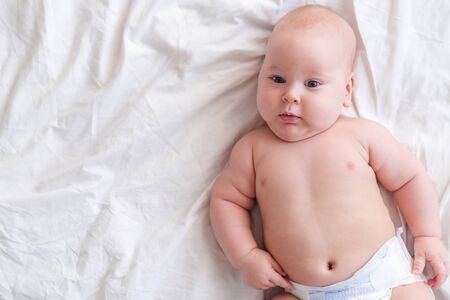 Adorable serious baby boy under white blanket in bedroom. Newborn child relaxing in bed. Family...