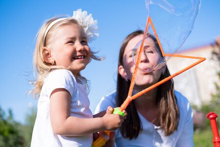 Happy mother and little daughter blow bubbles playing having fun outdoor in park at summer. Family lifestyle. Mom resting together on the green grassの写真素材