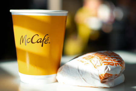 McCafe menu in McDonalds restaurant. Yellow cup of coffee and cheeseburger on table. Breackfast, time for coffee. FInland, Vantaa, 28feb2020.のeditorial素材