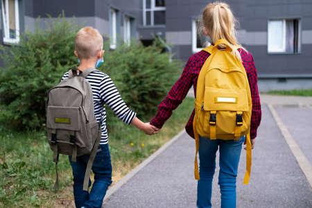back view Brother and sister going school after pandemic over. Kids wearing mask and backpacks...