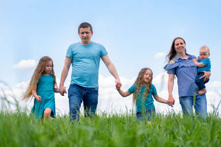 Big family dad, mom and three children walk on green grass against blue sky. Happy caucasian...