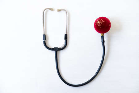 Creative Medical Christmas card stethoscope and red ball on white wooden background. Medicine new year flatly.の写真素材