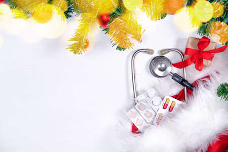 Medical banner with pills, gift present box, stethoscope and Christmas tree on white wooden background. Copyspace. Medicine new year flatly.の写真素材