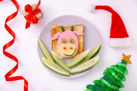 Funny sandwich with edible symbol of 2021 bull cow made from toast bread, sausage and cheese, cucumber Breakfast idea for kids. New Year Christmas food top view . holiday, celebration, food art.の写真素材