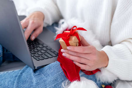 Christmas online shopping. Female buyer makes order on laptop. Woman buy presents, prepare to xmas, among gift boxes and packages. Winter holidays salesの写真素材