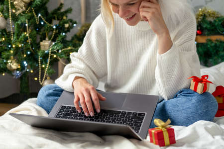 Christmas online shopping. Female buyer makes order on laptop. Woman buy presents, prepare to xmas, among gift boxes and packages. Winter holidays salesの写真素材