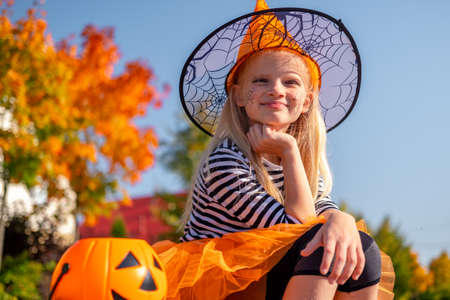 Halloween kids. Portrait smiling girl in witch hat with pumpkin candy bucket. Funny kids in carnival costumes outdoors.の写真素材
