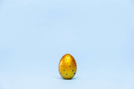 Happy Easter. One easter egg trendy colored gold on blue background. Copy space. Minimal style.の写真素材