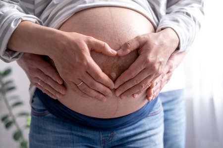 close up hands on mother and father making heart on pregnant big belly advanced pregnancy. Lover...