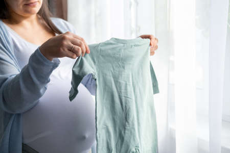 close up hands on pregnant mother holding baby clothes. Lover woman waiting child. Preparation for chillbirth, Girl big belly advanced pregnancyの写真素材