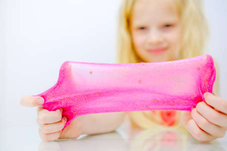 Blonde girl stretching pink glitter slime to the sides. Kids hands playing slime toy. Making slime. Copyspace. Selective focusの写真素材
