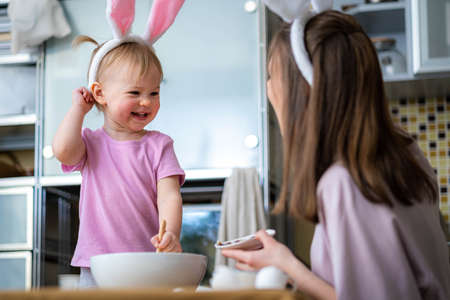Happy easter, Joyful family mom and daughter wearing bunny ears headbands gathering at table in...