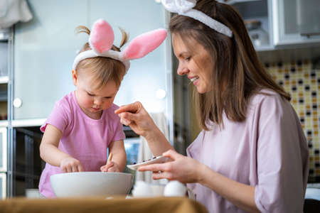 Happy easter, Joyful family mom and daughter wearing bunny ears headbands gathering at table in...