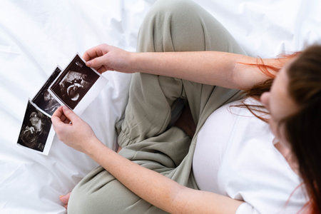 Top view cropped of pregnant woman looking ultrasound photo of fetus standing at home, young future mom waiting child first baby, pregnancy and motherhood conceptの写真素材