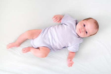 Newborn baby boy 3 months old lies in crib nursery with blue clothes on his back, looks at the...