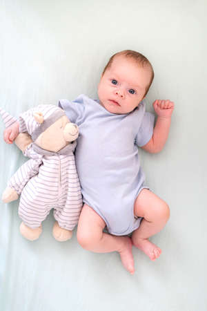 Newborn baby boy 3 months old lies in crib nursery with blue clothes on his back with teddy bear,...