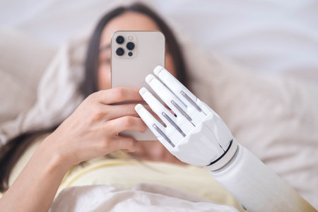Girl with bionic arm using phone, reading social media and chatting in bed, woman with disability learning or working online remotely from homeの写真素材