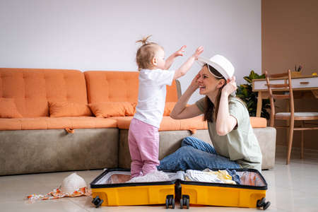 Mother and baby girl with yellow suitcase baggage and clothes, family ready for traveling on...