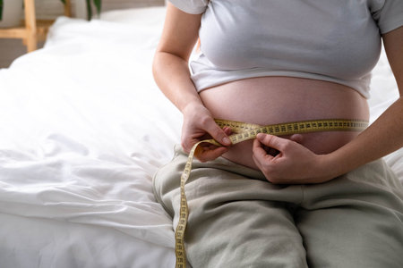 Young woman measuring her pregnant belly with centimeter tape. Preparation for childbirth, Girl big belly advanced healthy pregnancy.の写真素材
