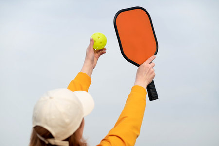 back view pickleball game woman player, hands over blue sky hitting pickleball yellow ball with paddle, outdoor sport leisure activityの写真素材