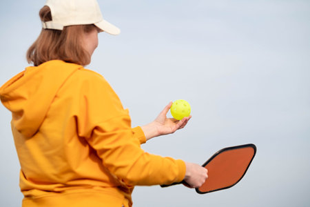 back view pickleball game woman player, hands over blue sky hitting pickleball yellow ball with paddle, outdoor sport leisure activityの写真素材