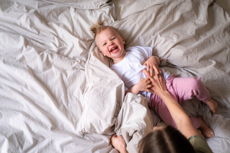 Mother and daughter laughing having fun together on bed, Little baby girl and mommy playing at home.の写真素材