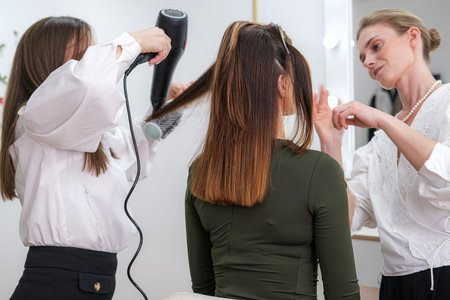 Woman having her hair styled by hairdresser in a salon, skilled hairdresser in bustling beauty salon environment, where various transformations occur, stylist does makeup, four hands workの写真素材