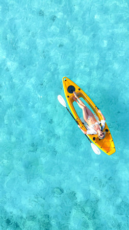 woman in a bikini relaxes on a yellow kayak floating on clear turquoise sea, top-down view from above, peaceful moment in tropical paradise, summer holiday, maldives, travel, holidays, vacationの写真素材