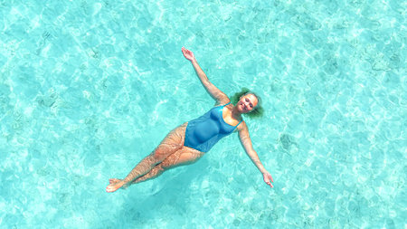 Asian Woman floating in crystal clear turquoise water, arms stretched, enjoying relaxation on...