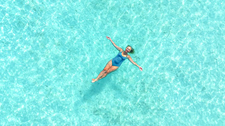 Asian Woman floating in crystal clear turquoise water, arms stretched, enjoying relaxation on...