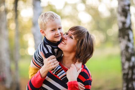 Mother with her son in her arms hugging communicate, play, fall, parkの写真素材