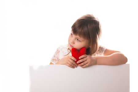 Serious baby girl with red heart in hand, the concept of Valentine's Day, white background, a place for an inscriptionの写真素材