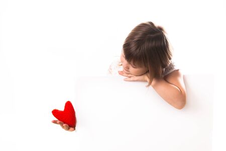 pensive baby girl with red heart in hand, the concept of Valentine's Day, white background, a place for an inscriptionの写真素材