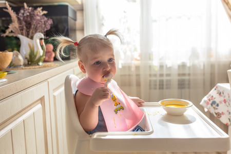 sad Naughty funny with bunches baby eating independently alone in the high chairの写真素材