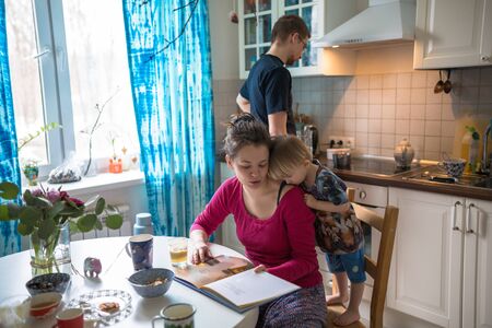 Caucasian mother and son toddler having fun in the kitchen reading bookの写真素材