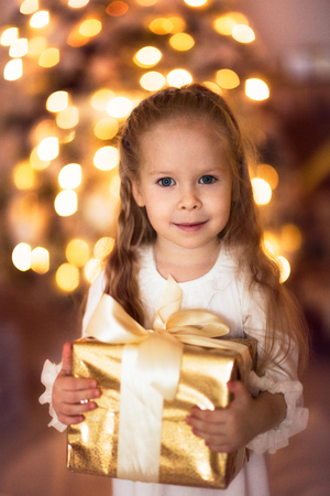 Caucasian girl with blond long hair with a Christmas gift, golden lights, the concept of the New Year and Christmas lifestyleの写真素材