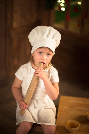 Gir cook with a rolling pin to stretch the dough, the concept of childhood, mother's helpers, independence. Dark background, lightsの写真素材