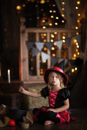 little witch in costum and hat conjure above pot, childhood halloween, dark backgroundの写真素材