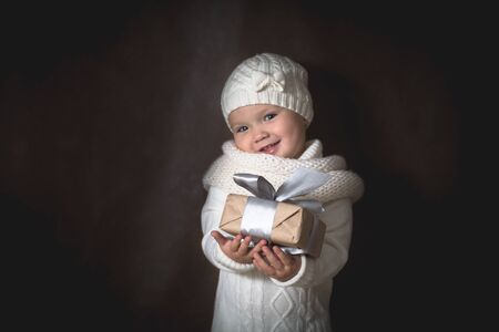 Retro girl in a knitted hat, scarf and sweater with Christmas present, brown background, concept...