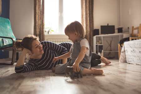 young pregnant mother with dreadlocks, and her son play  on floor, lifestyle, Real interior, toning, selective focusの写真素材