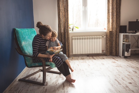 young pregnant mother with dreadlocks, and her son play and reading a book on sofa, lifestyle, Real interior, toning, selective focusの写真素材