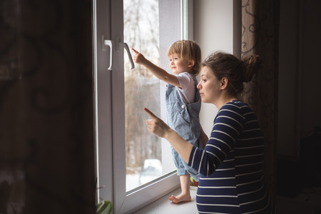 young pregnant mother with dreadlocks and her son playing, hugging, kissing the window real interior, lifestyle, toning, selective focusの写真素材