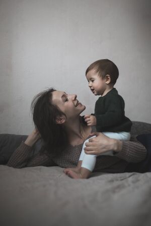 Shaggy young mother and baby in a knit sweater hugging and  playing on the bed, the concept home...