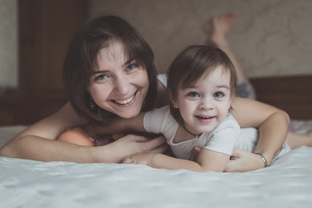 young dark haired mother and daughter Toddler playing, cuddling in bed, lifestyle, pastel colors, selective focusの写真素材