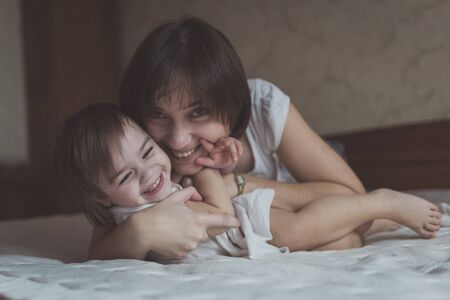 young dark haired mother and daughter Toddler playing, cuddling in bed, lifestyle, pastel colors, selective focusの写真素材