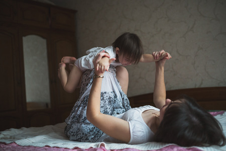 Mother hugging and playing with his toddler daughter in bed, lifestyle, pastel colors, selective focusの写真素材