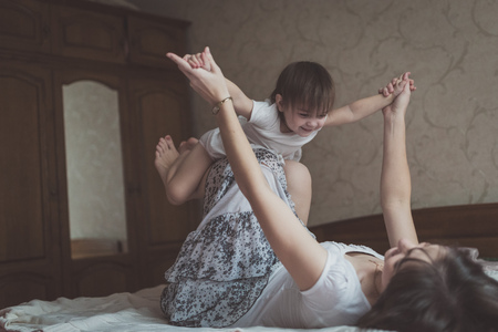 Mother hugging and playing with his toddler daughter in bed, lifestyle, pastel colors, selective focusの写真素材