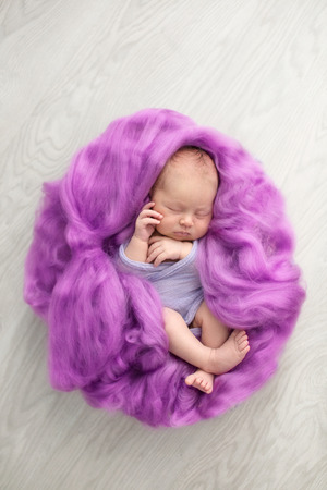 sleeping newborn girl in the purple violet pink wool background, close-upの写真素材